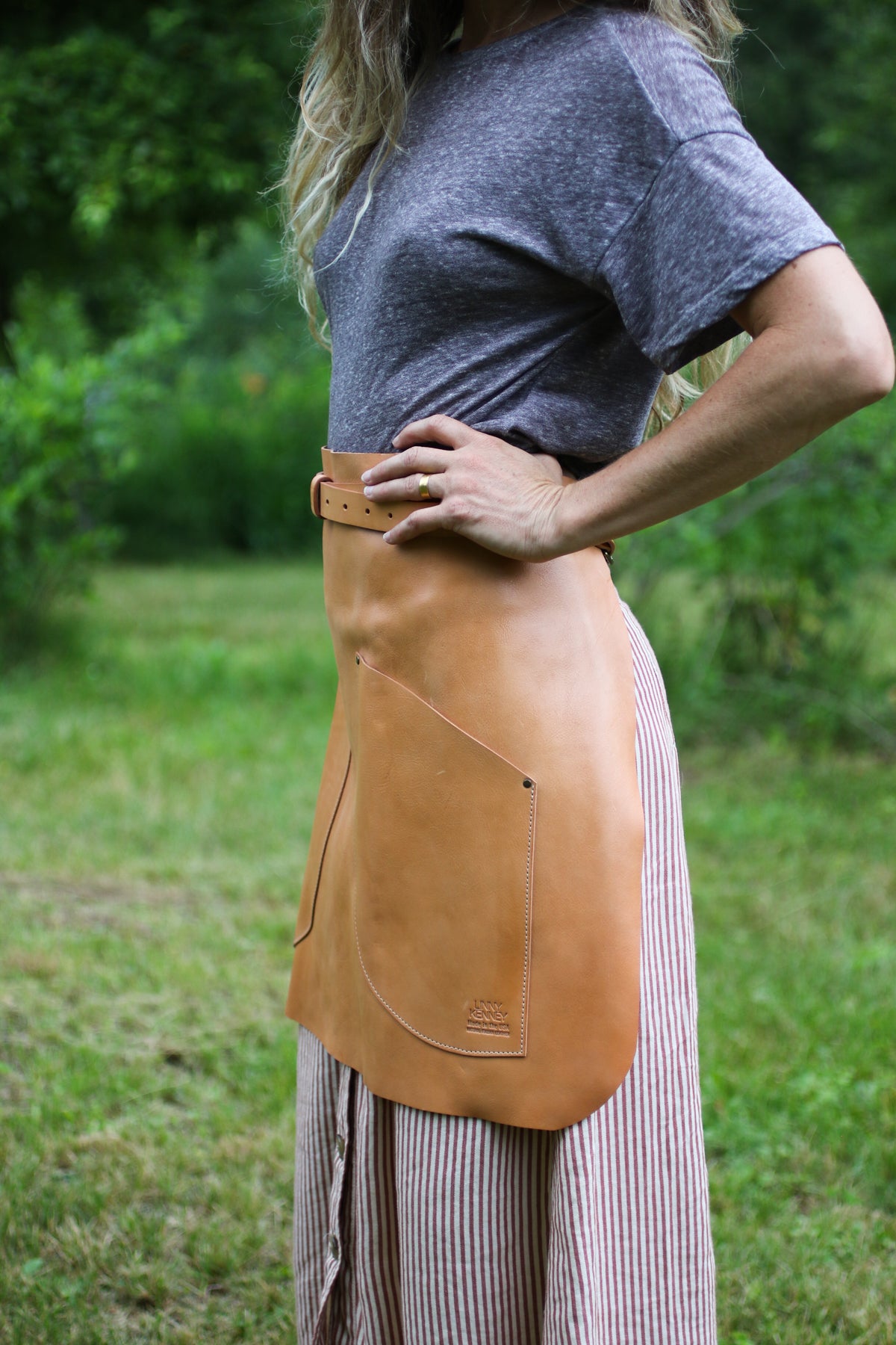 Person wearing a tan leather apron outdoors with greenery in the background